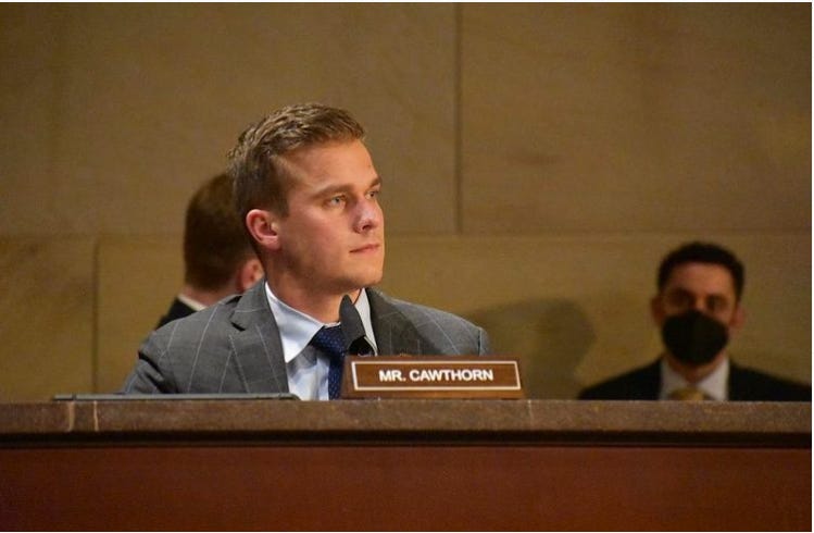 Madison Cawthorn is shown from the chest up, seated, wearing a gray suit and white tie, looking away from the camera. A name plaque reading "Mr. Cawthorn" appears in front of him.