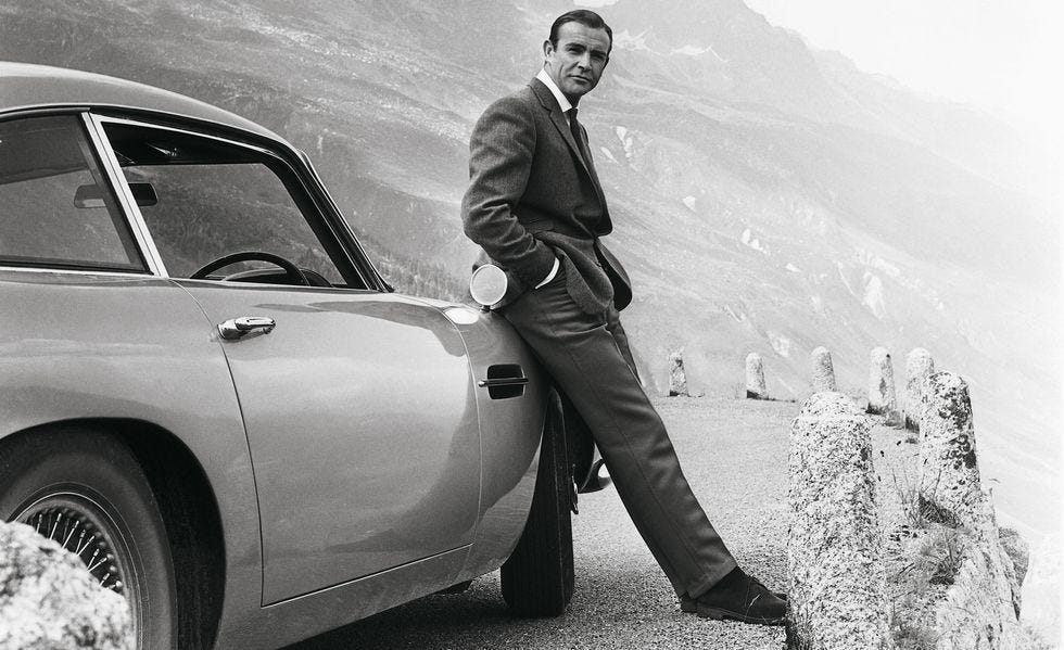 This black-and-white promotional image from 1964's Goldfinger shows Sir Sean Connery as James Bond leaning against 007's Aston Martin DB5 while parked on a mountain pass in Switzerland. This black-and-white promotional image from 1964's Goldfinger shows Sir Sean Connery as James Bond leaning against 007's Aston Martin DB5 while parked on a mountain pass in Switzerland.