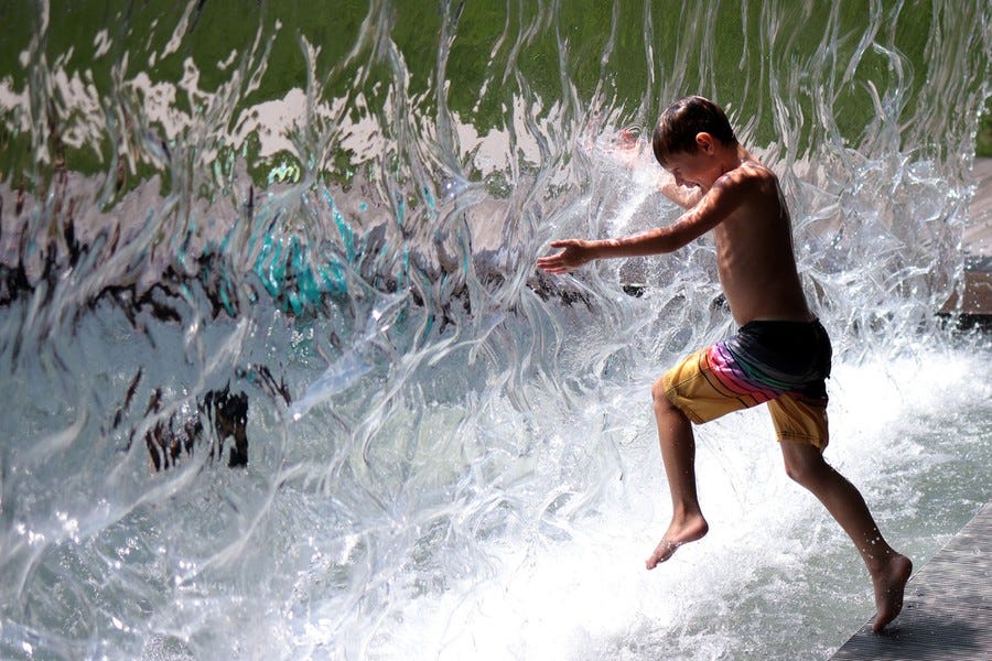 A child splashes through a curtain of water in a fountain.