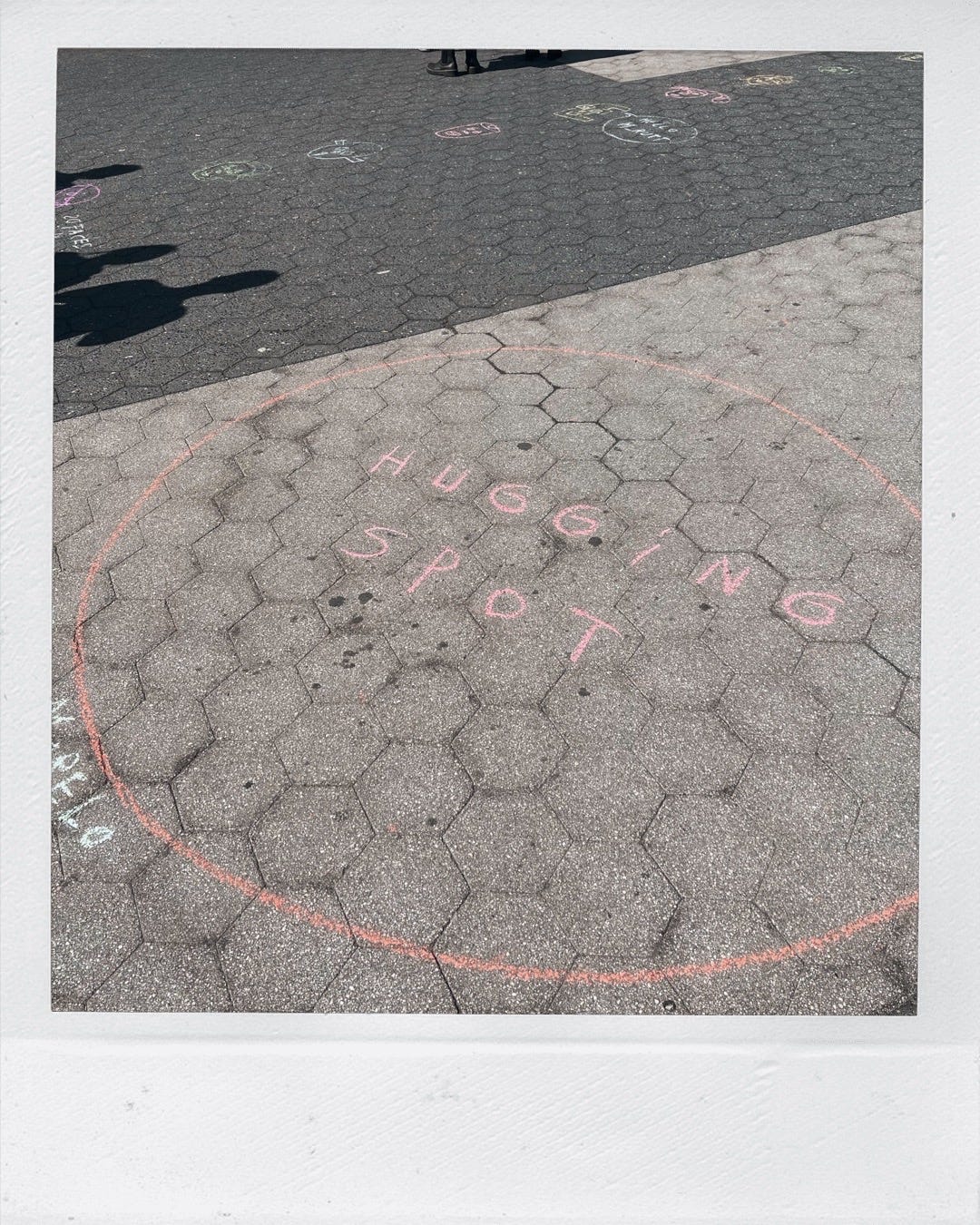 photo of a "hugging spot" written in chalk on the ground. Top left corner shows some of Morelo's chalk faces