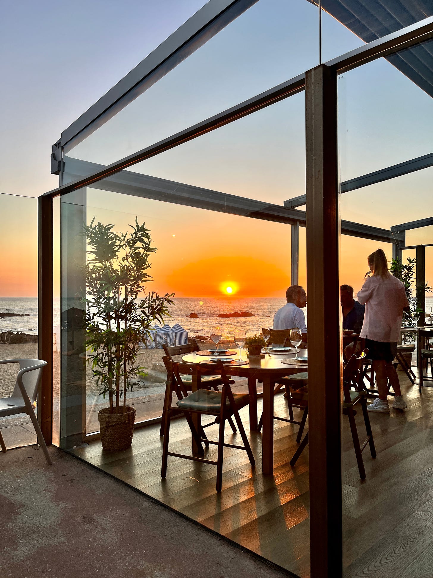 Image: a gorgeous scene of sunset over the Atlantic Ocean, with diners enjoying wine and conversations, overlooking the beach. 