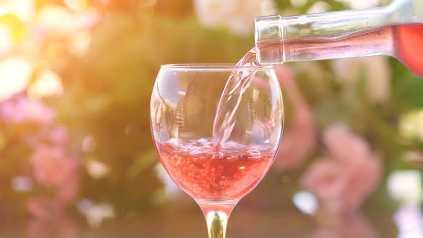 Pouring a glass of cold rose wine, green garden background