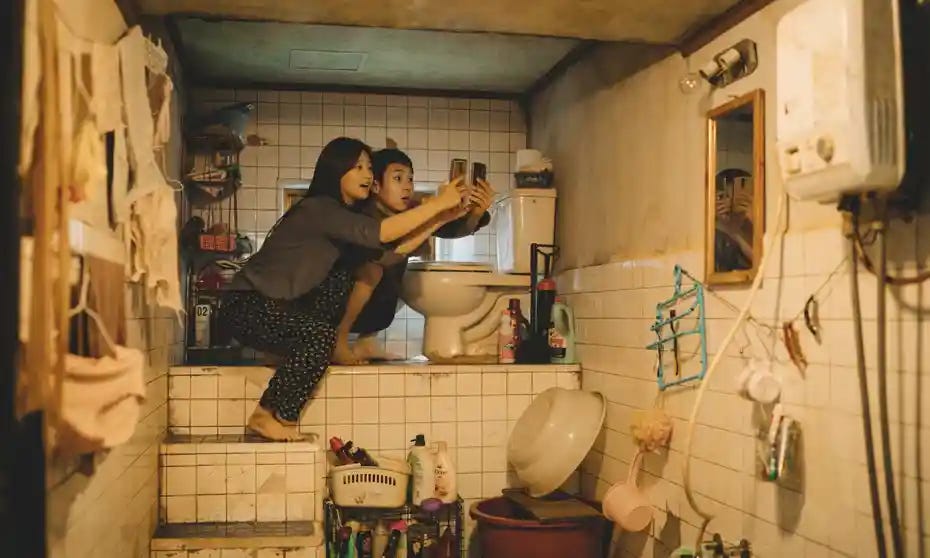 Two siblings hold up their cell phones to try to get wifi in their basement apartment bathroom in the film Parasite.