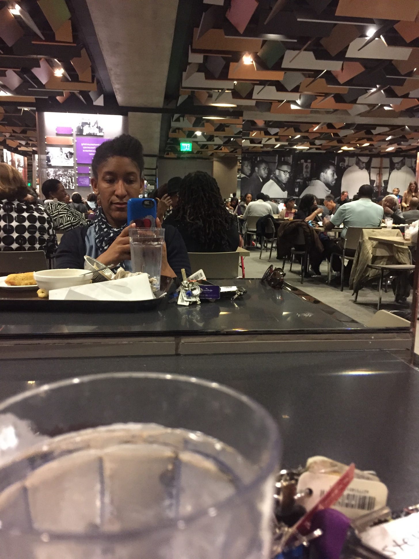 Inside the cafeteria of the National Museum of African-American Culture and History. Kristen is taking a mirror selfie of the other wall of the room, featuring a print of the Greensboro 4 engaged in the sit-in process