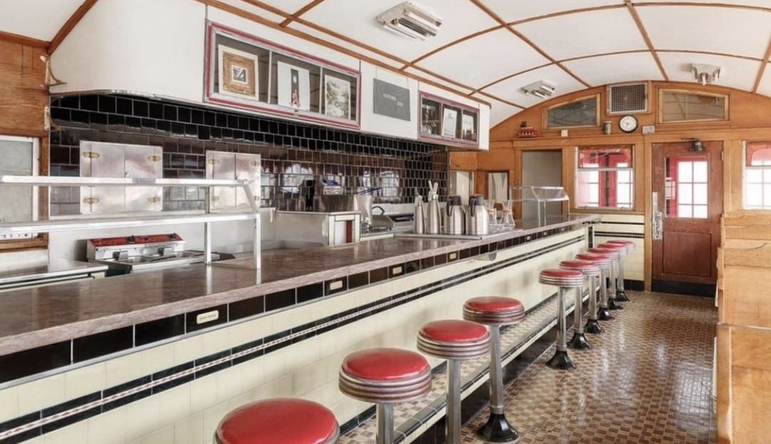 A diner interior, with a row of stools in front of a tiled bar