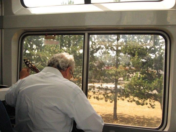 A man tuning his guitar in the Amtrak lounge car