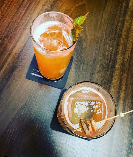 Foto tirada de cima pra baixo mostrando dois copos de drink em cima de uma mesa de bar de madeira