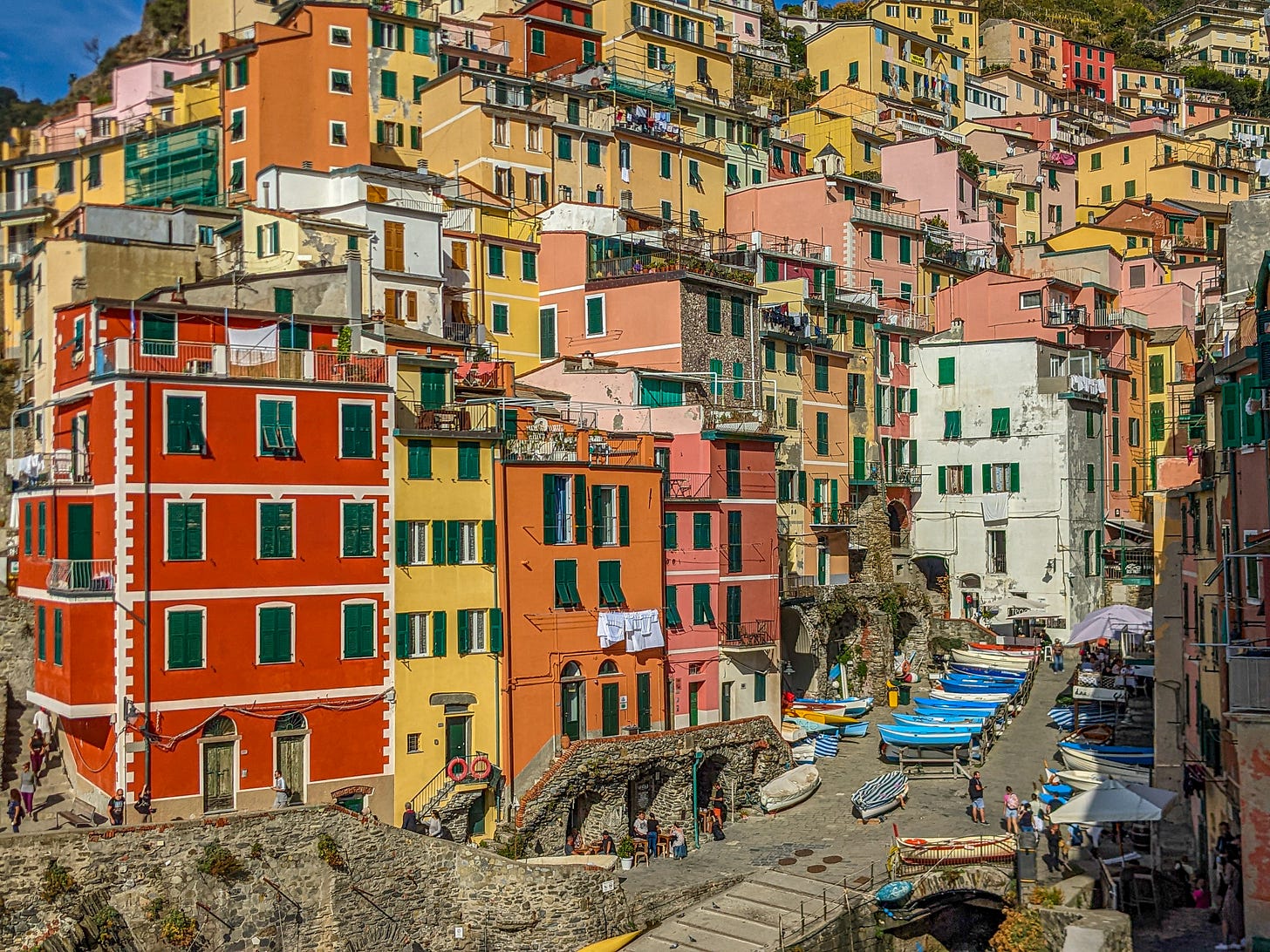A view of Riomaggiore from the water, red, yellow, pink, and orange buildings marching up the hillside. 