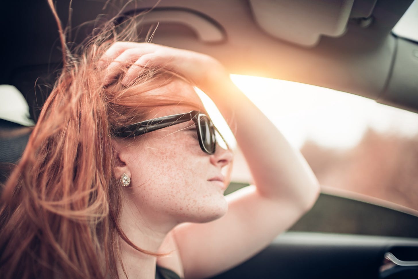 A red haired woman drives down the road while the sun sets.