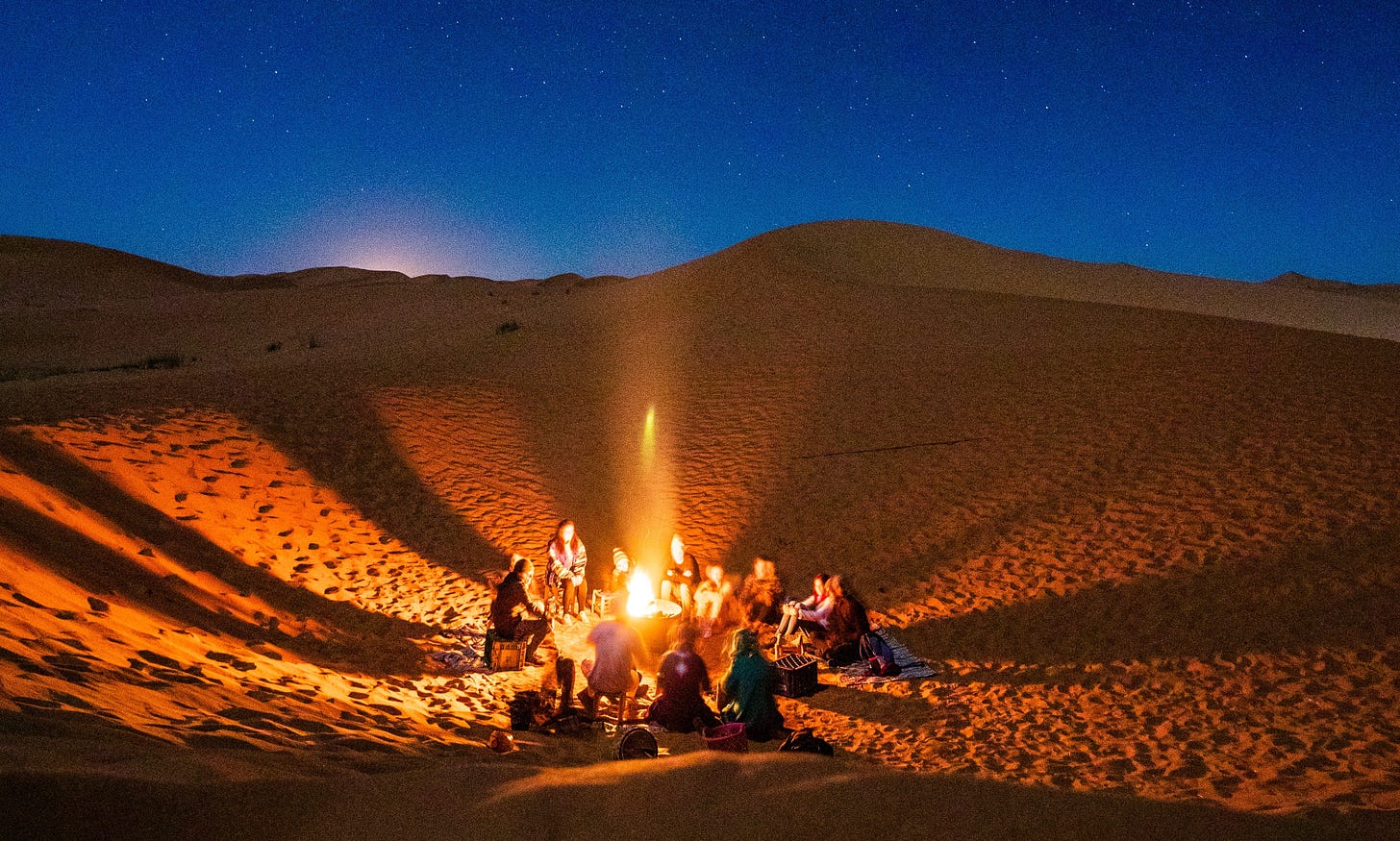 People sitting around a bonfire in the desert at night.