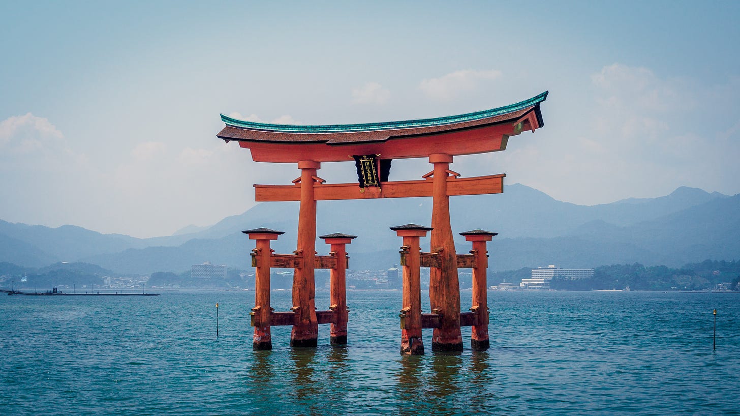 A famous Japanese “floating” shrine, made of orange-painted wood, and surrounded by water, with mountains in the background.
