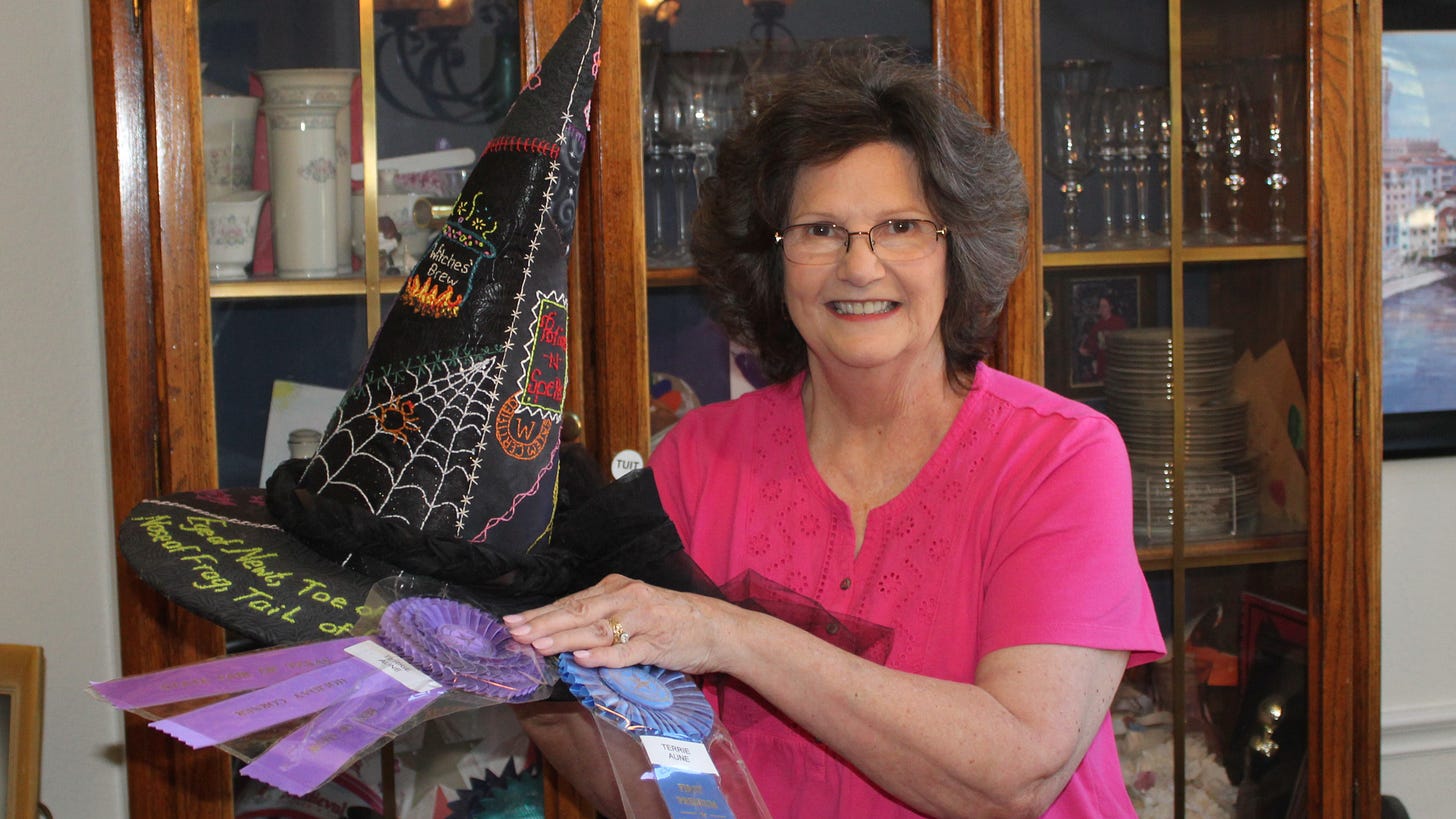 Terrie Aune displays her award-winning black witch's hat covered with embroidered phrases and cobwebs