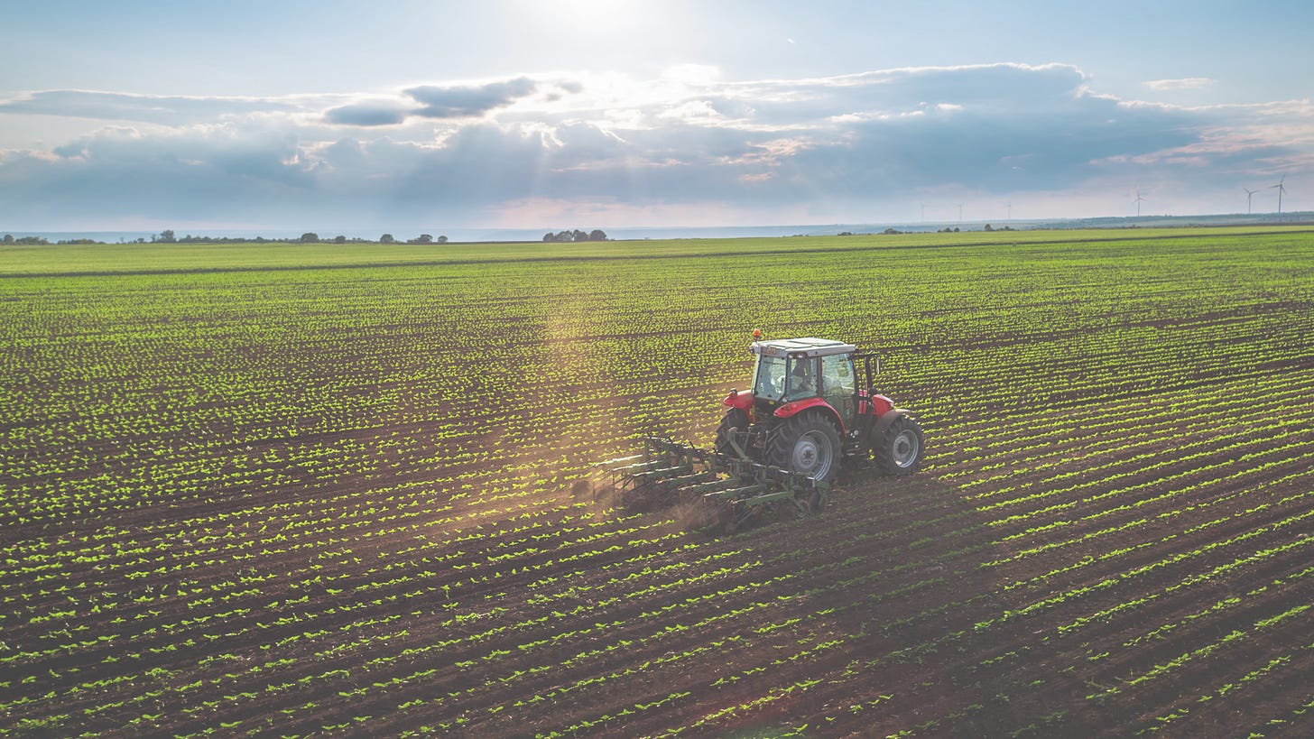 An aerial view of a large agricultural field with rows of crops and a farm vehicle in the background