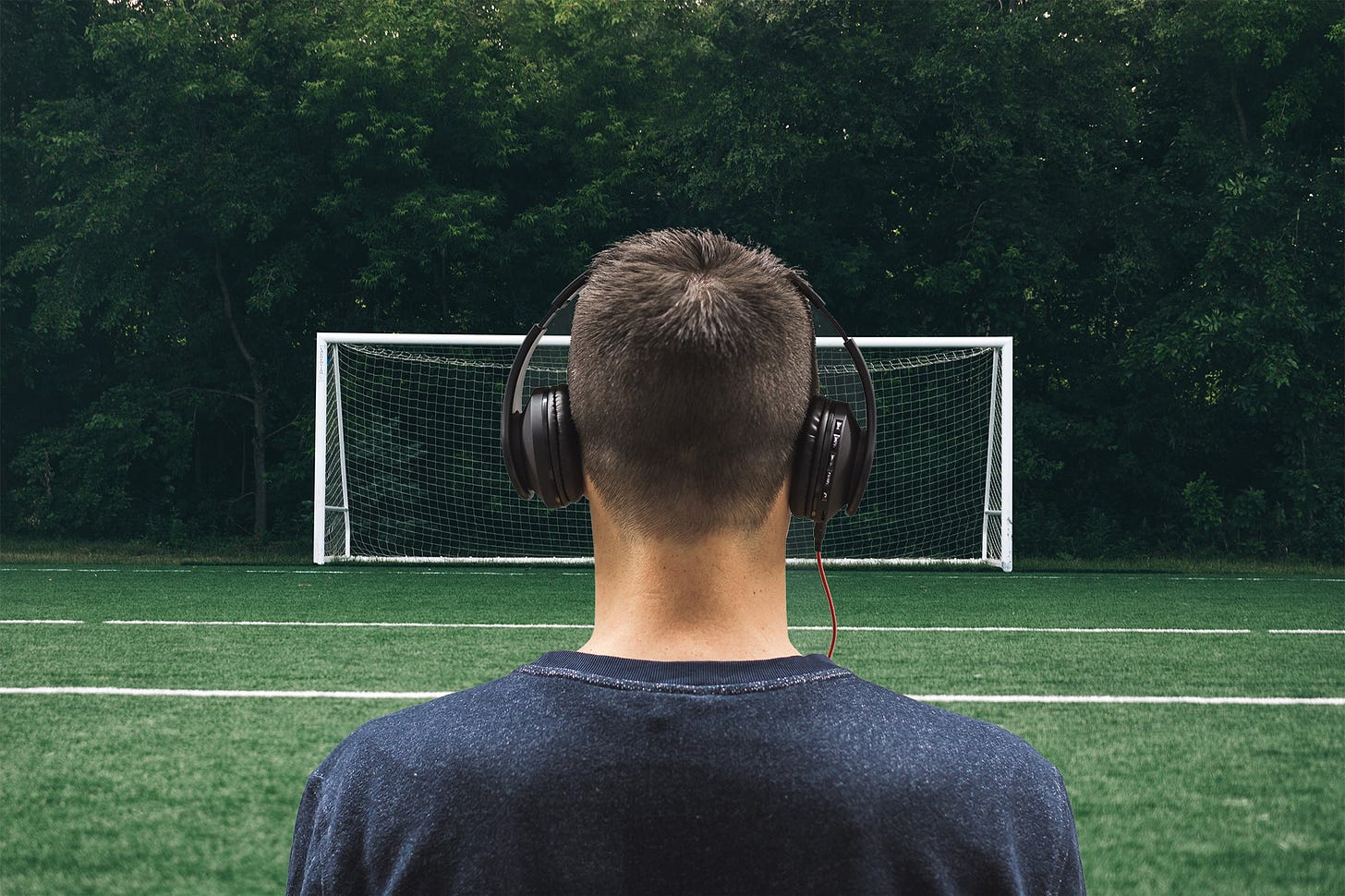 man wearing headphones facing soccer goal