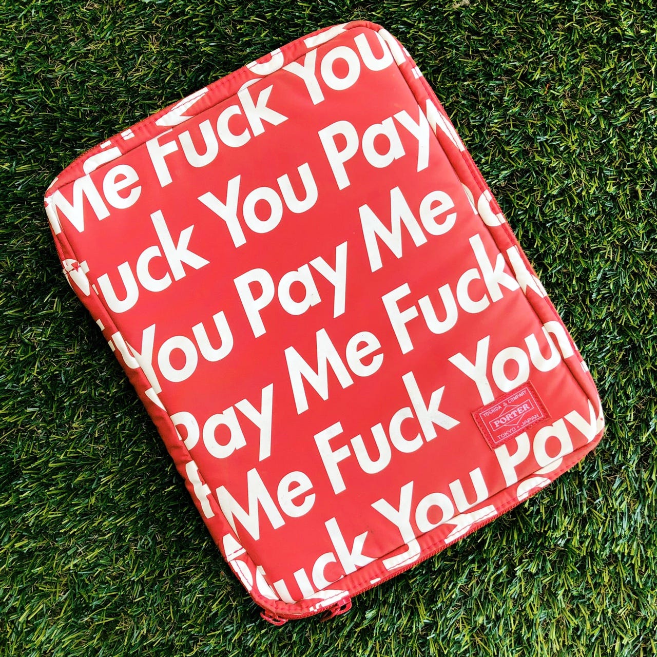 A red backpack with text, in white Futura, reading 'Fuck You Pay Me.'
