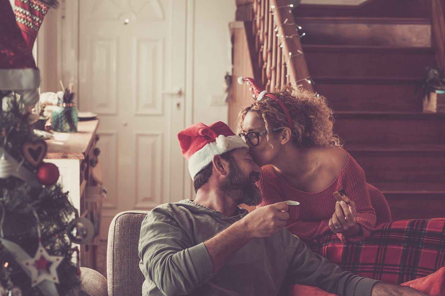 A couple surrounded by holiday decorations kiss happily at home.