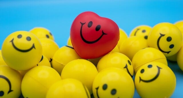 a pile of foam balls painted with smiling yellow faces and one with a smiling red heart
