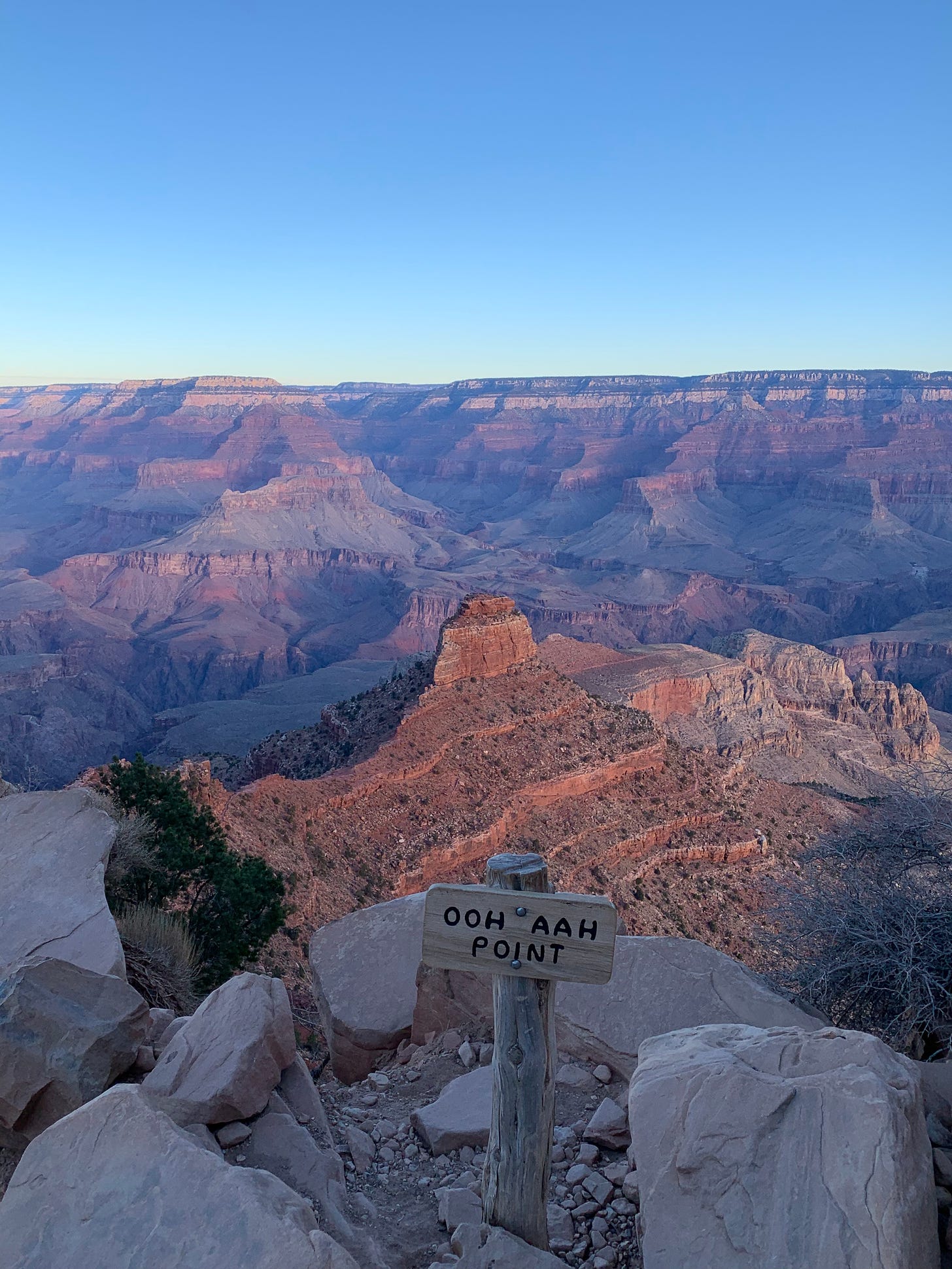 A sign says "Ooh Aah Point" above the Grand Canyon at dawn