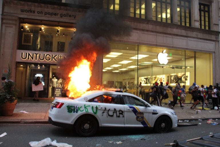 A police car burns outside a looted Apple store in Center City.