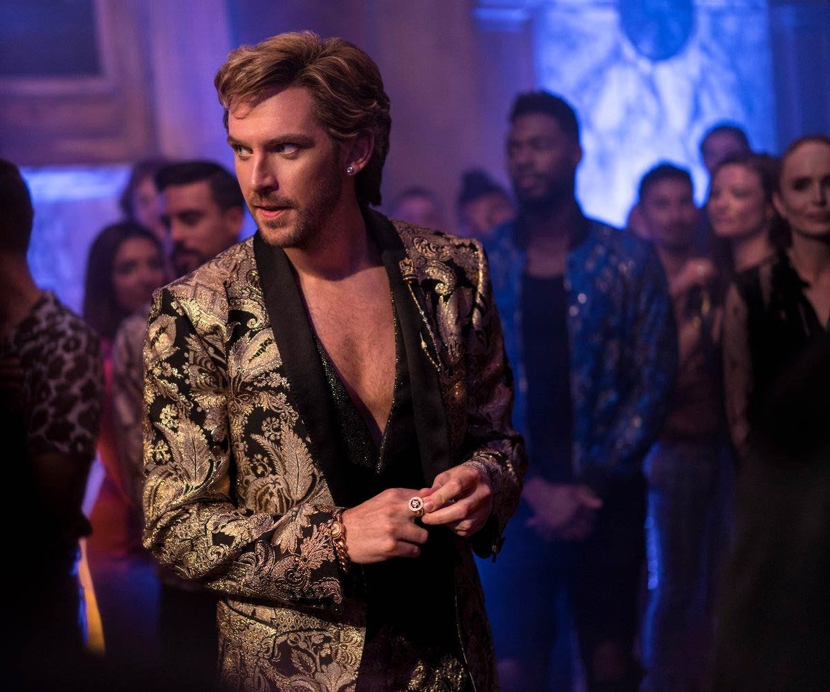Dan Stevens as the character Alexander Lemtov in the film Eurovision. He is wearing a gold embroidered jacket with no shirt on underneath, and is looking away from the camera.