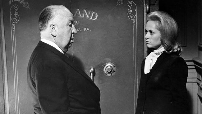 Set photo from Marnie. Alfred Hitchcock and Tippi Hedren stand in front of a bank safe.