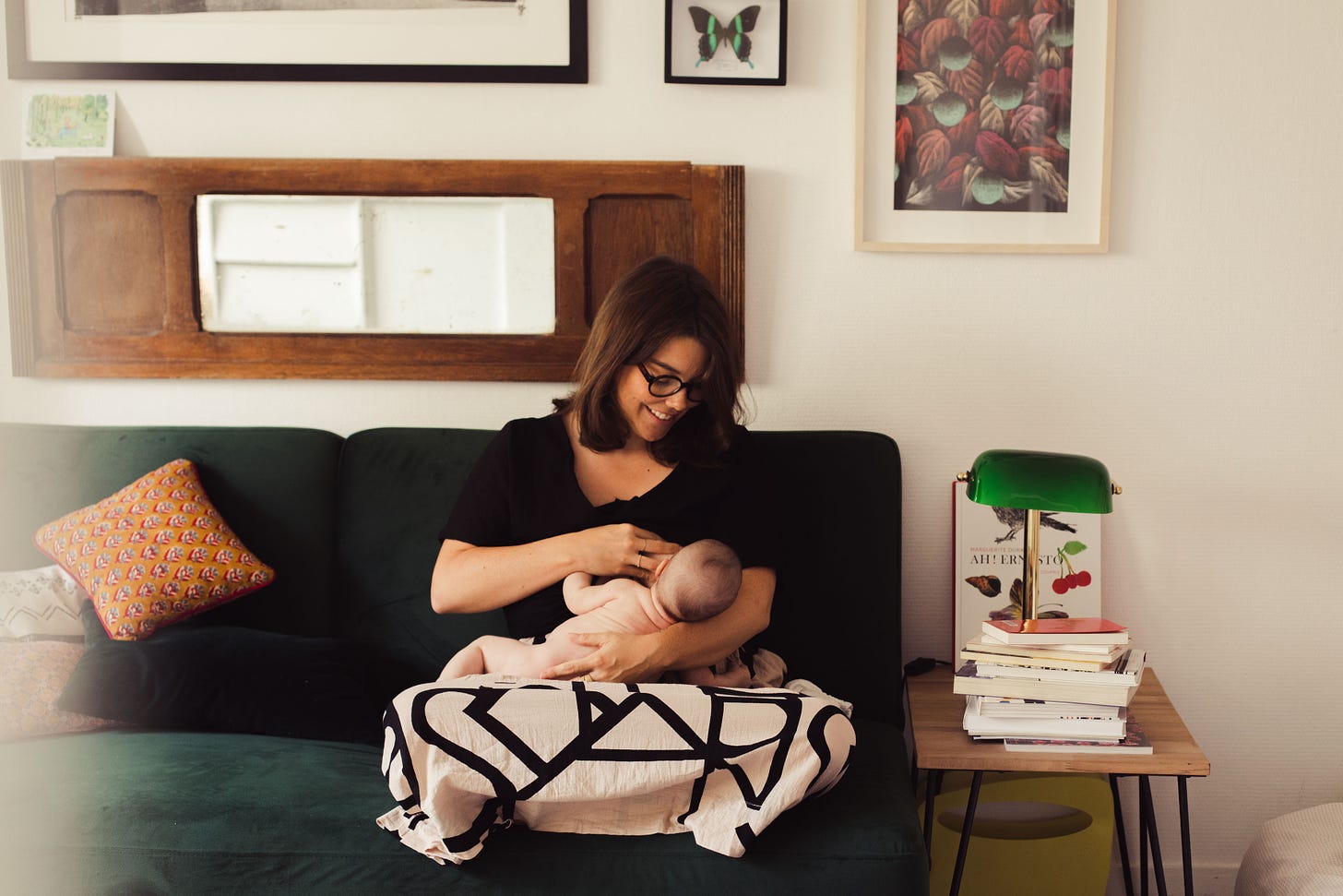 Une femme assise sur un canapé allaite un nourrisson. Elle le regarde en souriant.