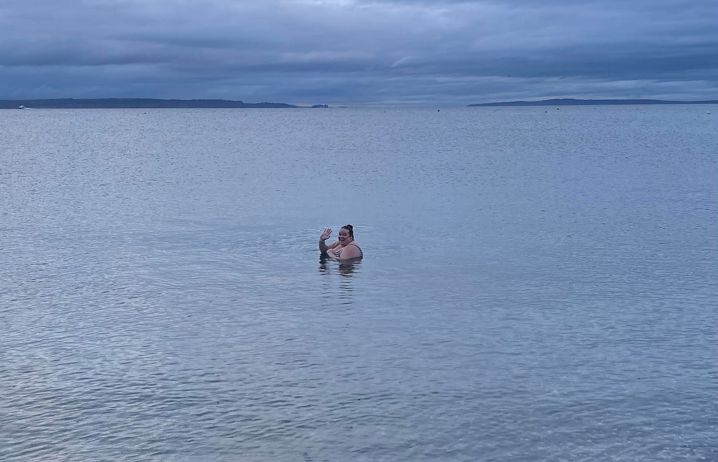 photo of Christina submerged in water up to her shoulders, outside in Puget Sound, waving to camera