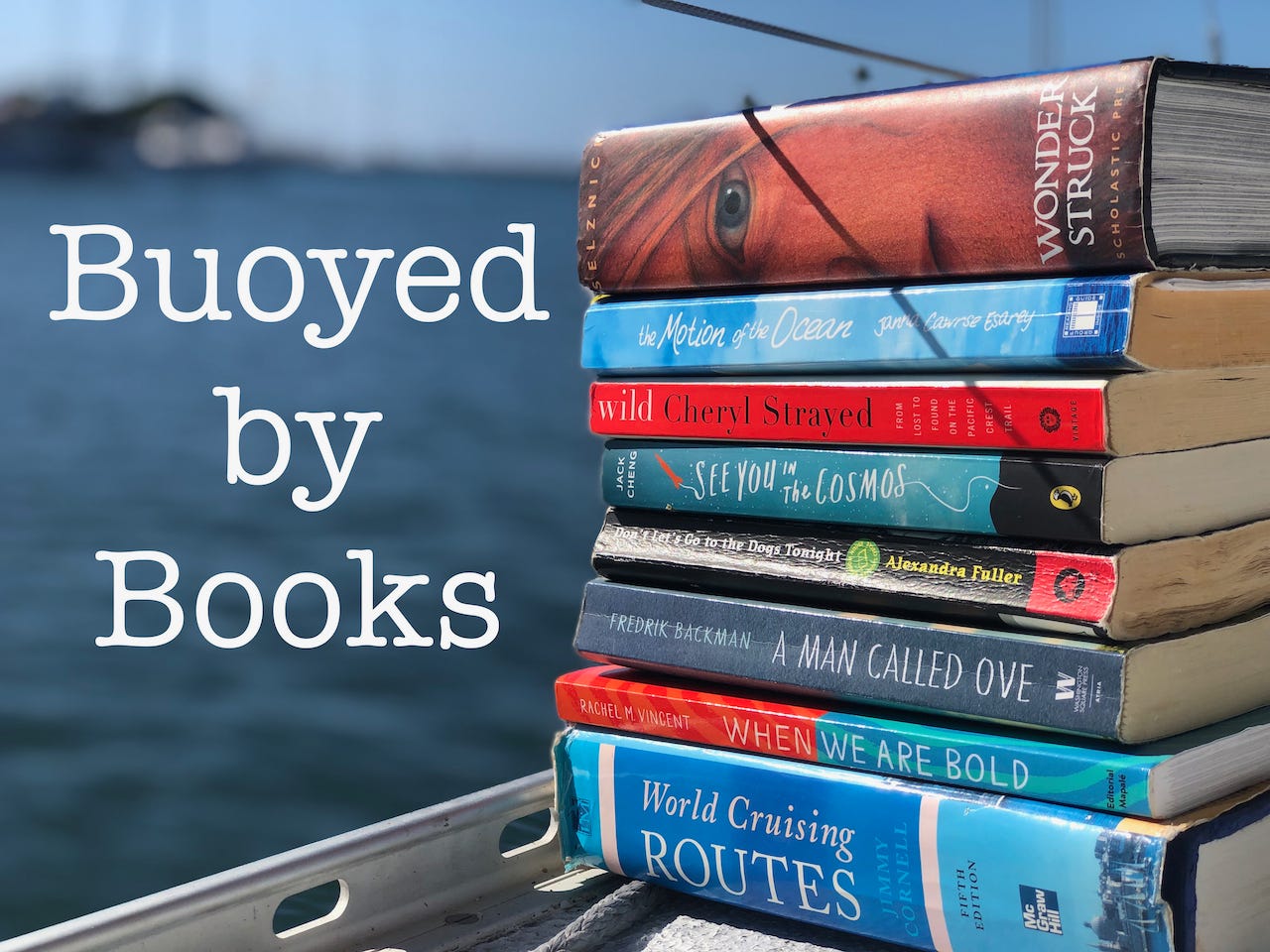 A stack of books on a sailboat's deck with text that reads Buoyed by Books.