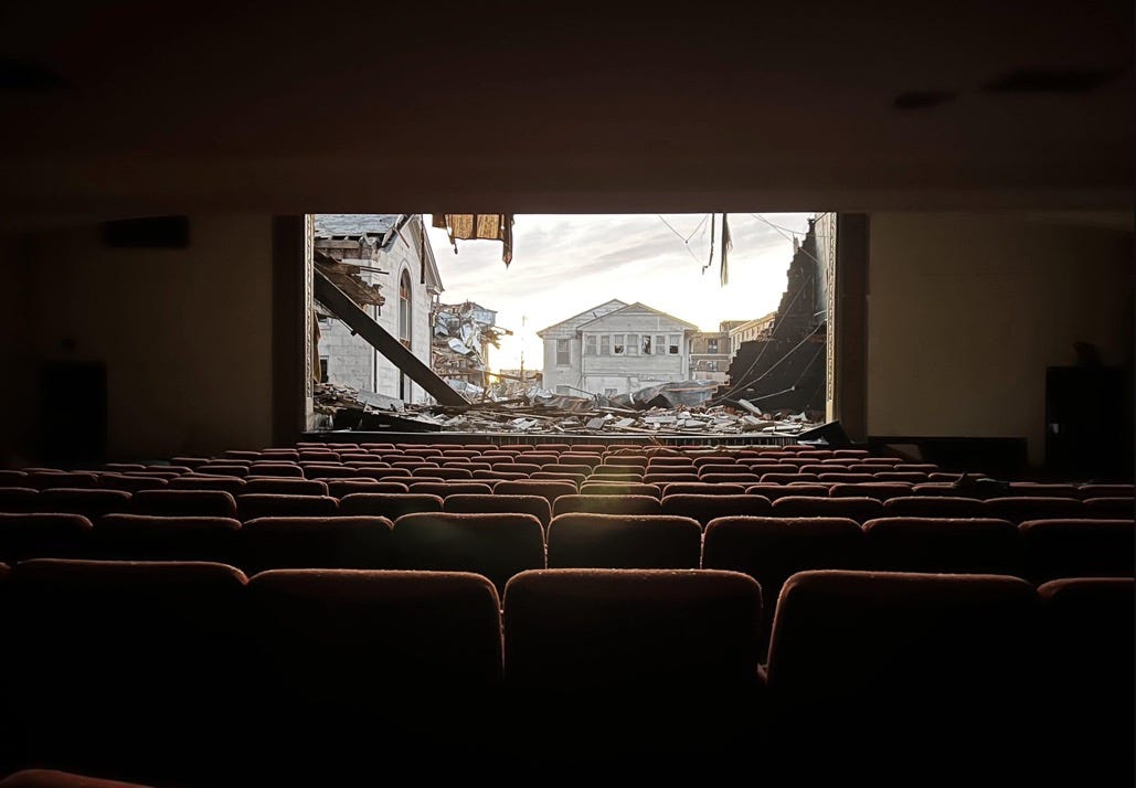 An empty movie theater with the screen torn away, showing the ruins of a town beyond.
