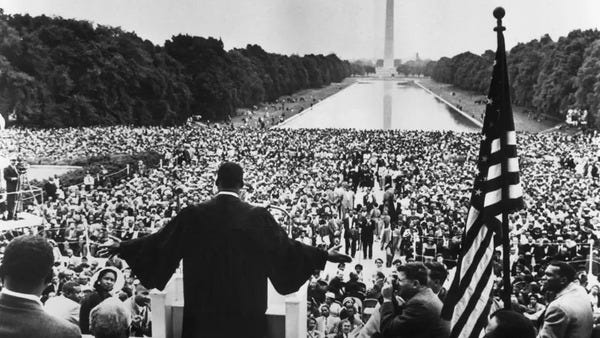 A shot from behind the lectern of Martin Luther King Jr. addresses a massive crowd, which fills the National Mall in Washington DC.