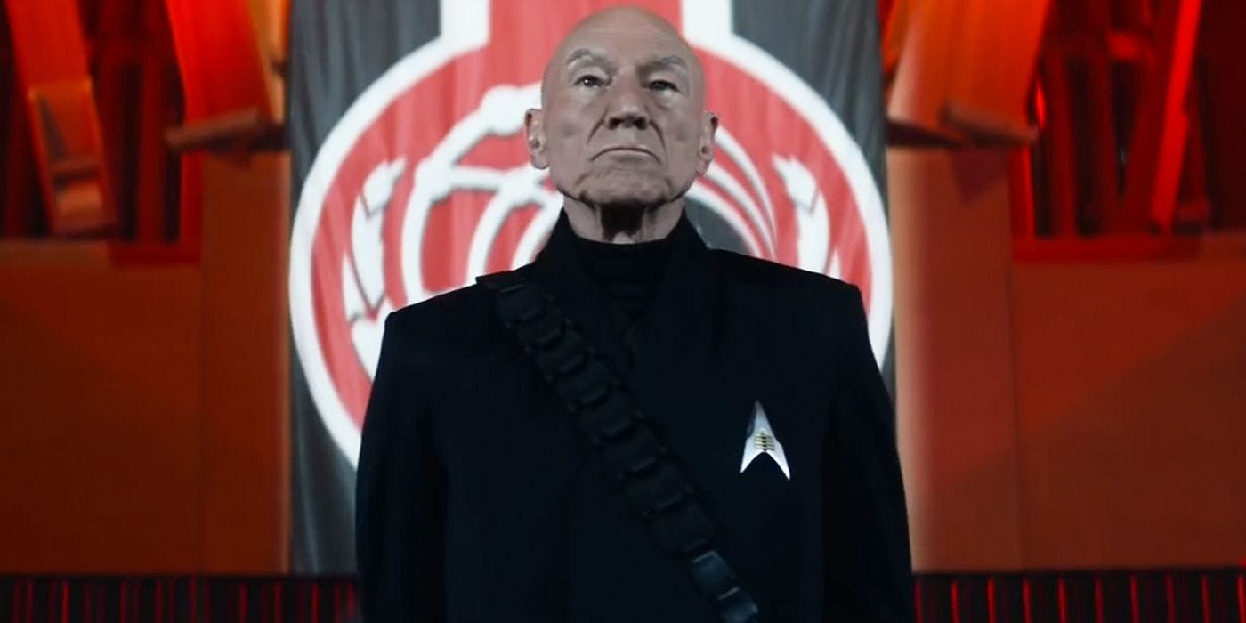 This image shows General Jean-Luc Picard (played by Patrick Stewart) in "Penance," the second episode of Star Trek: Picard's second season. PIcard's face scowls, he wears an all-black uniform with the Confederation's delta-shaped combadge, and stands in front of the Confederation's black-red-and-white flag. This image shows General Jean-Luc Picard (played by Patrick Stewart) in "Penance," the second episode of Star Trek: Picard's second season. PIcard's face scowls, he wears an all-black uniform with the Confederation's delta-shaped combadge, and stands in front of the Confederation's black-red-and-white flag.