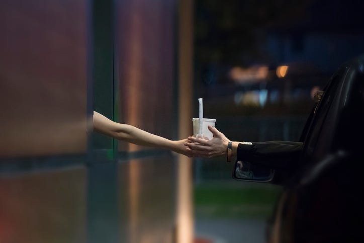A drink is passed from a fast-food drive-through window to a car's driver