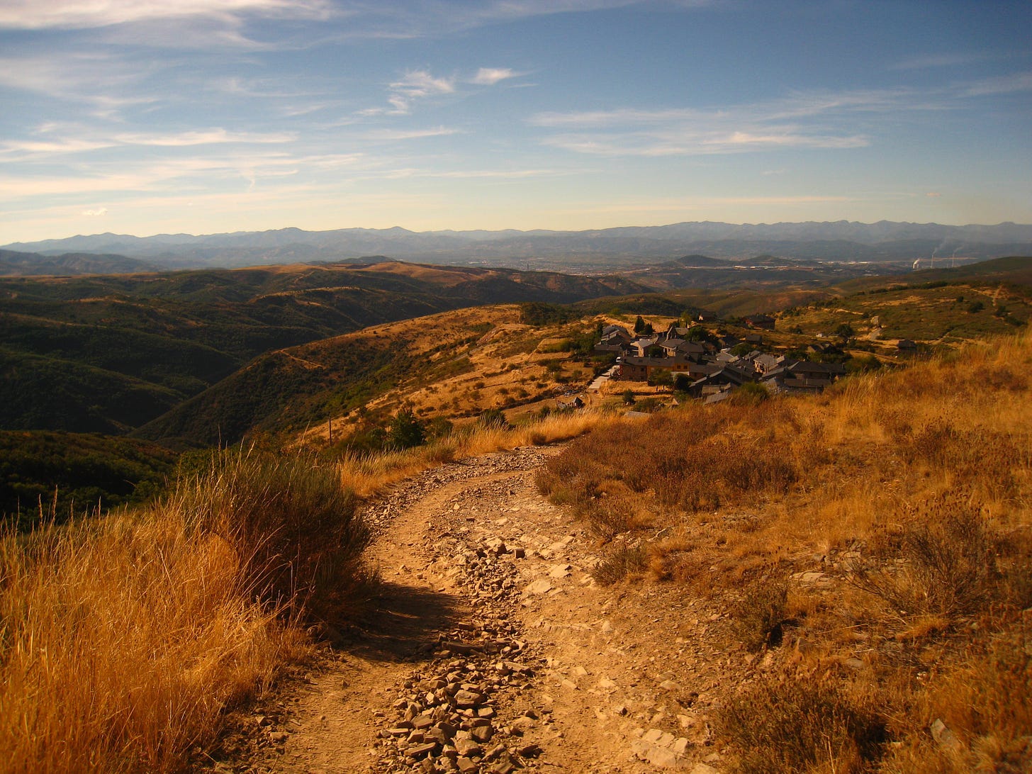 A stone hiking path stretches out into the distance over rolling, grassy hills in the golden glow of sunset.