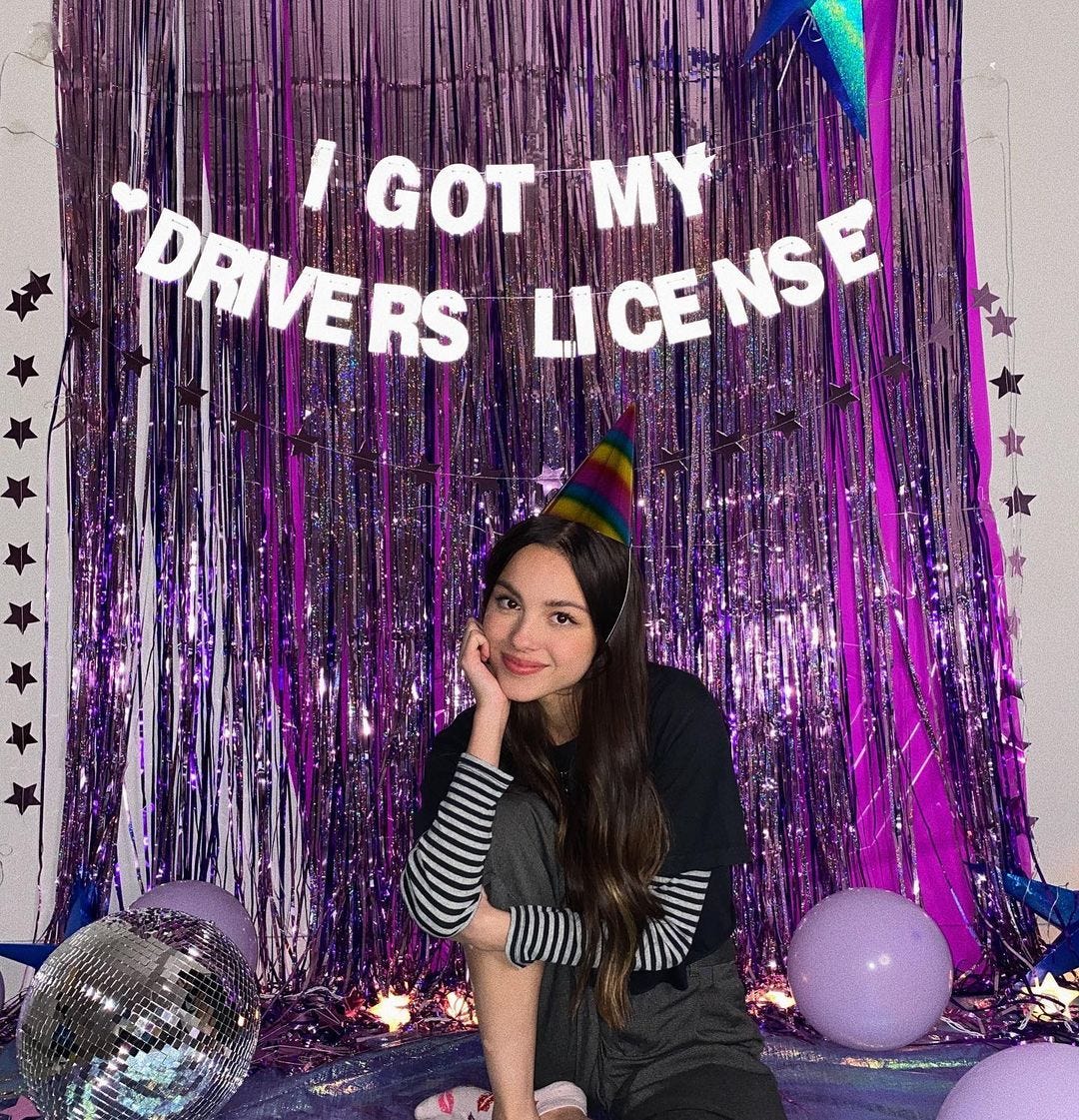 Olivia Rodrigo in front of a wall that says "I got my Drivers License"