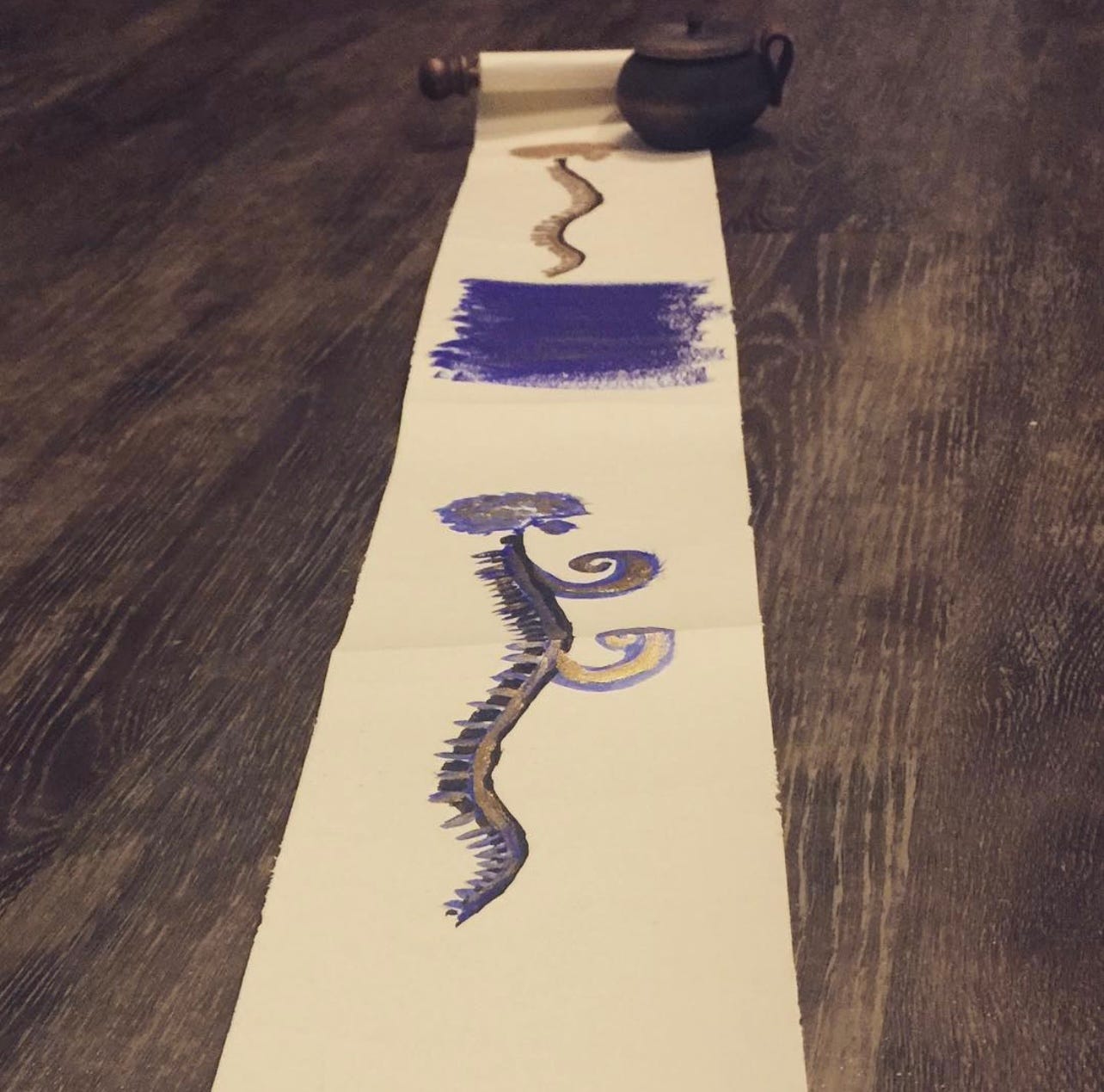 unfurled scroll with two spinal cord drawings, one with ultramarine strokes beneath and one with two tails. a small inkwell carved from walnut holds the scroll open at the far end