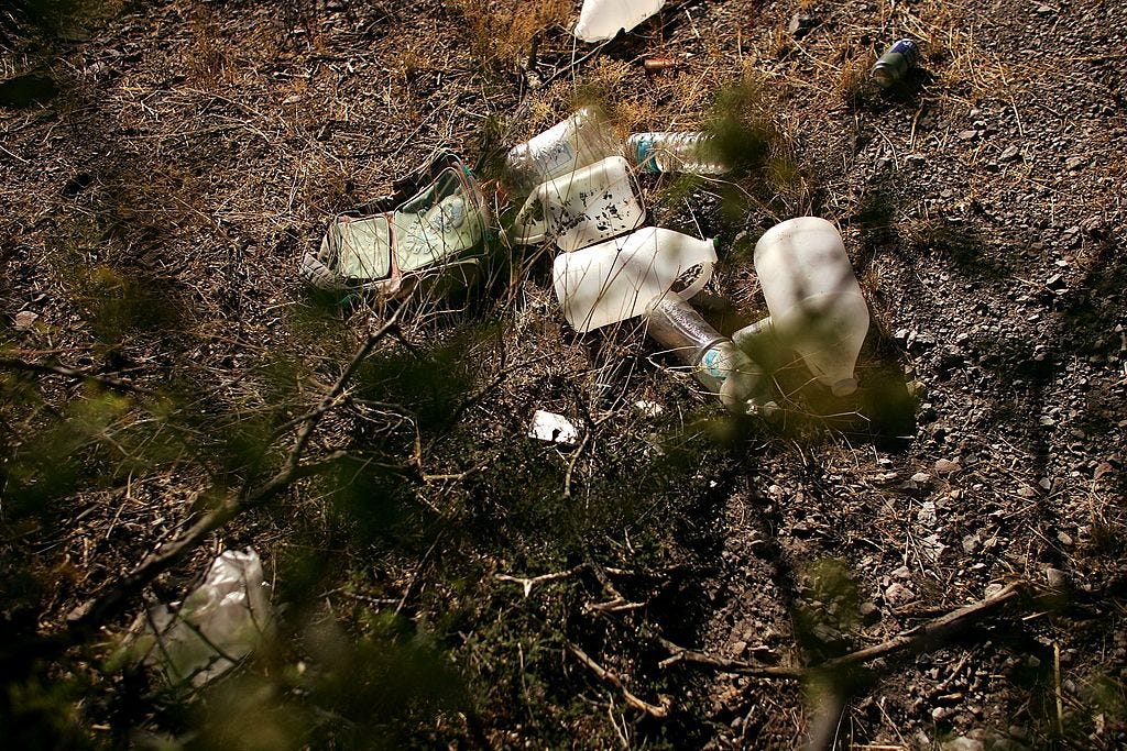 A photo of water jugs and bottles scattered on the desert ground with brush in warm yellow light