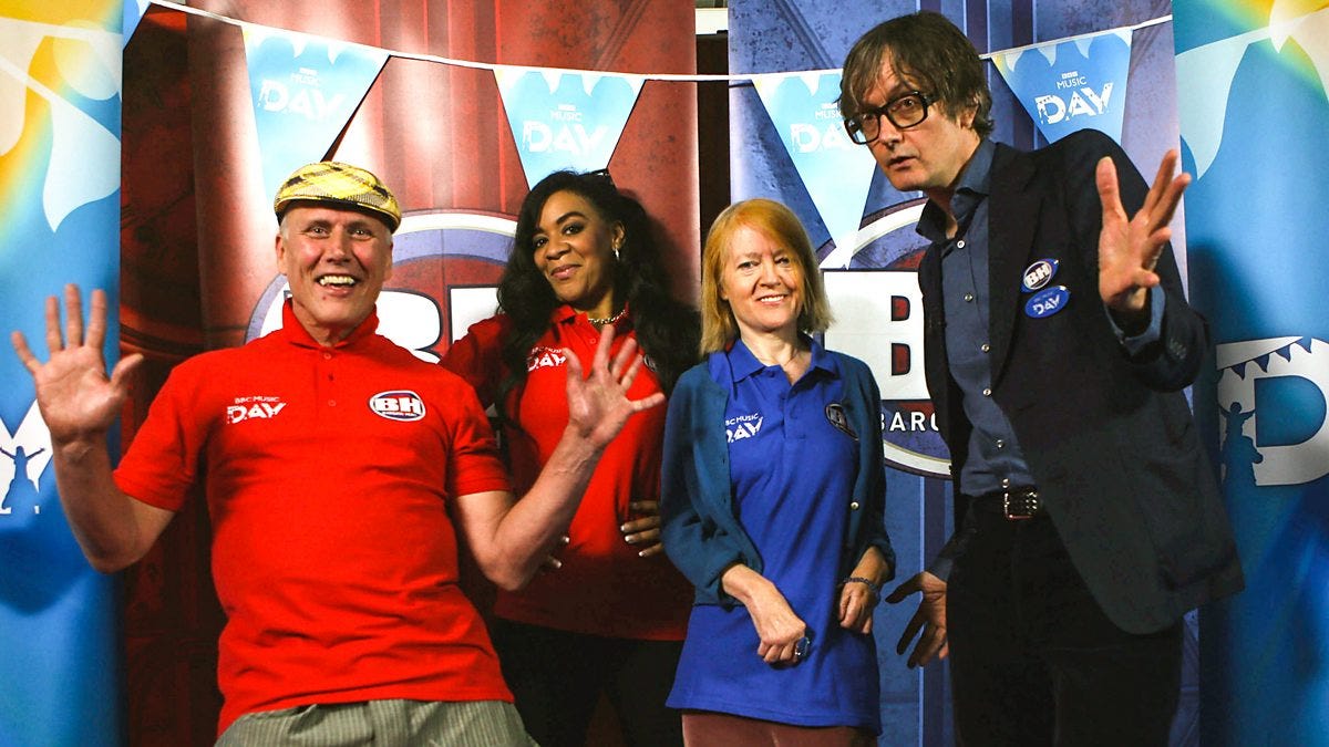 In the picture you can see four contestants. Bez from the band Happy Mondays is wearing a yellow cap and red shirt. Rowetta from Happy Mondays is wearing a red shirt. There is a contestant with red hair wearing a blue shirt. She is stood next to Pulp's Jarvis Cocker who is also wearing blue.