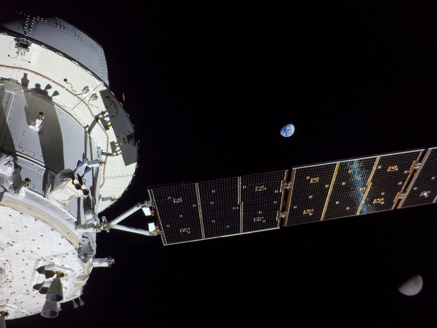 The Artemis capsule and solar array in the foreground, with the blue marble of Earth in the background and the moon in the lower right corner.