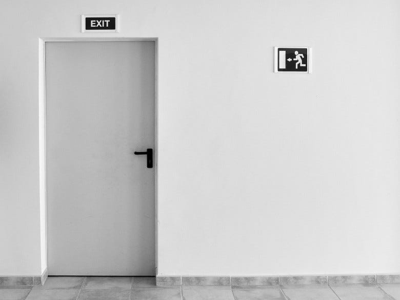 A white wall with a door and an exit sign