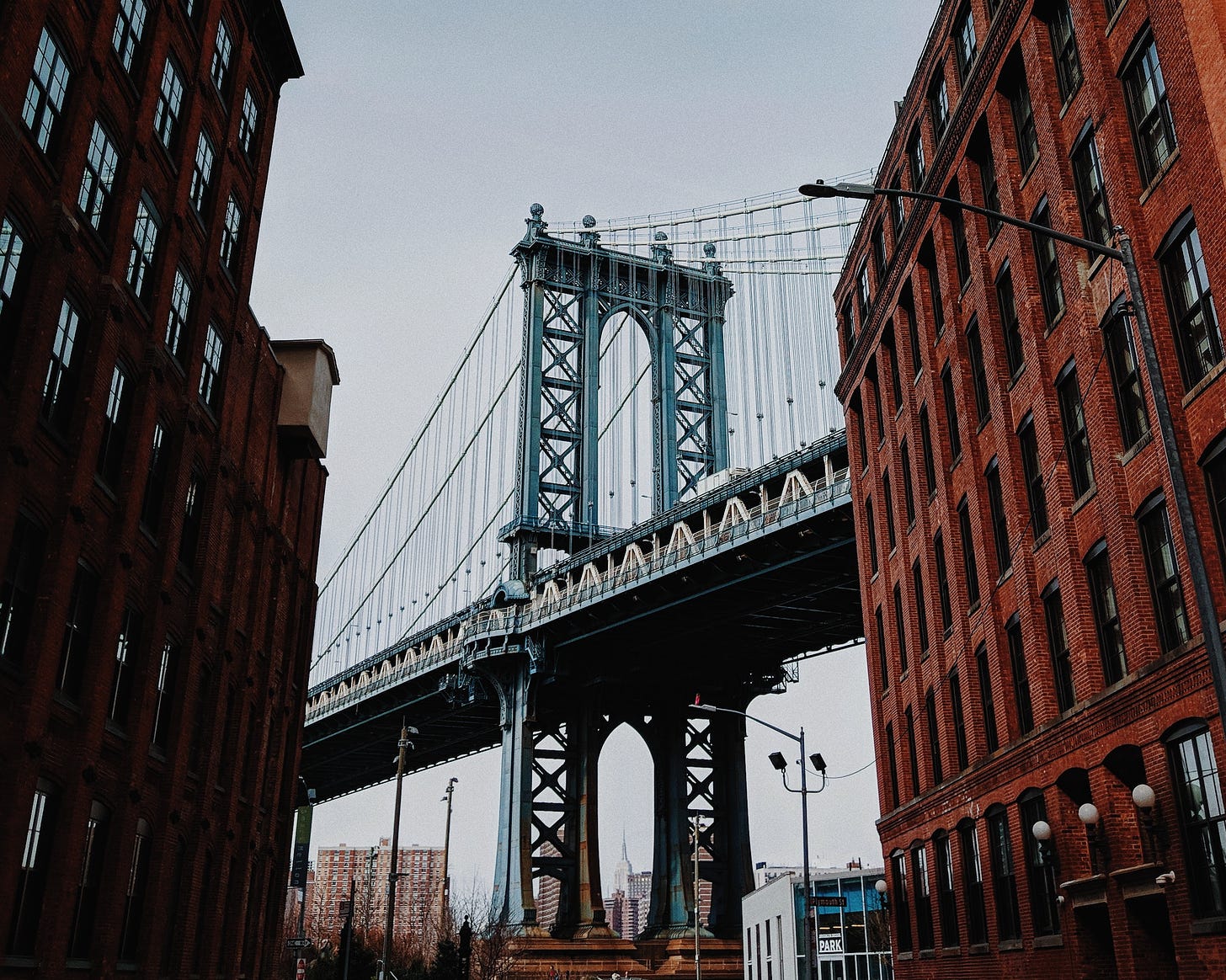 Photo of the Brooklyn Bridge between two brick buildings.