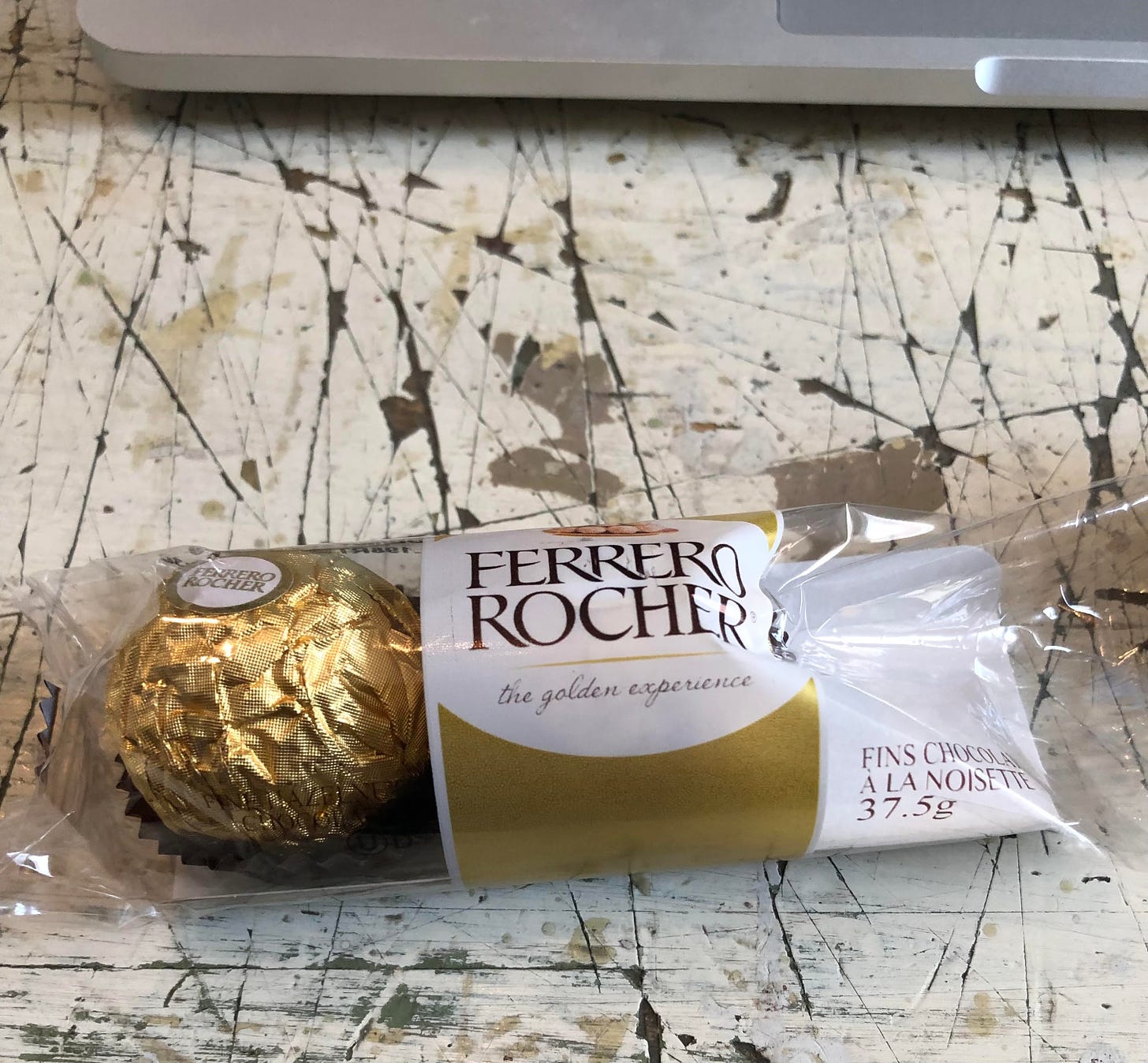 A pack of three Ferrero Rocher chocolates on a desk. One has been eaten. 