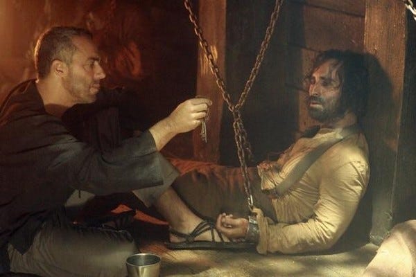 The Man In Black (Titus Welliver) holds up a key for Ricardo (Nestor Carbonell), who is haggard and chained up in the hold of a ship.