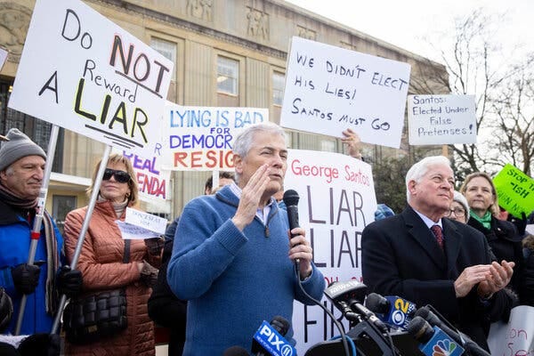 Robert Zimmerman, a Democrat from Long Island, holds a microphone in front of a crowd of people. They hold signs that say “Do not reward a liar” and “We didn’t elect his lies.”