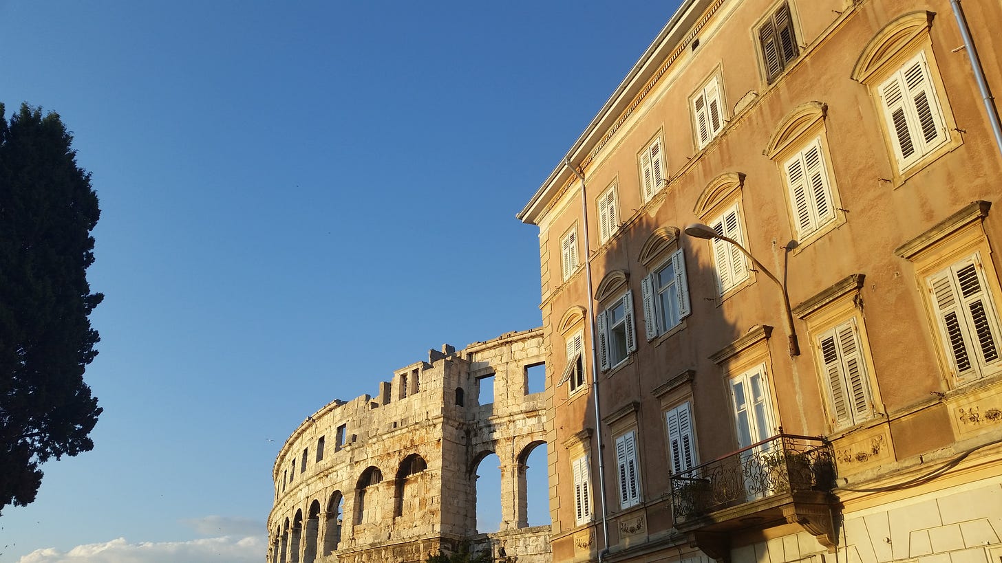 A random picture of Pula, Italy. There's a tree, ruins of an ampetheatre, and an old building