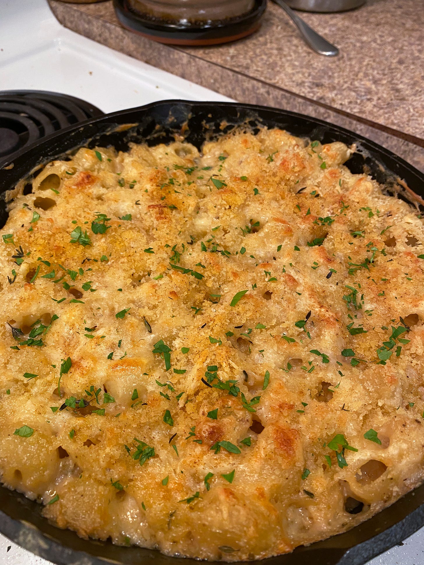 A cast-iron pan full of baked, browned mac & cheese with breadcrumbs, thyme, and parsley on top.