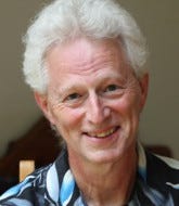 A smiling white man with gray hair in a blue patterned shirt. 