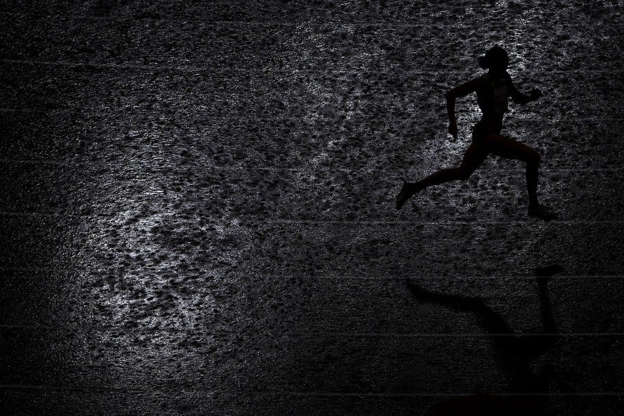 The silhouette of a runner is seen on a rain-soaked track.