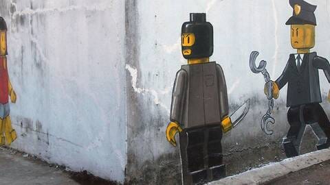 A Banksy like painting depicting a would-be masked Lego robber aiting around a corner for a potential female Lego victim, while a Lego policeman moves in for apprehension.