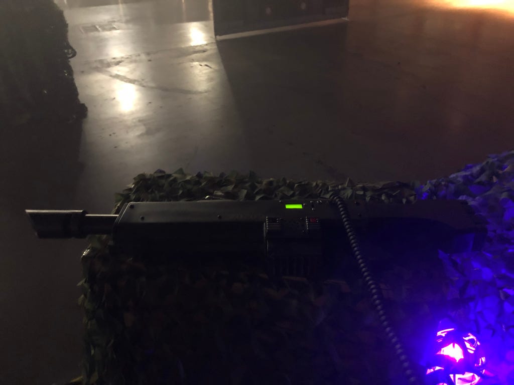 A futuristic-looking gun resting on a crate covered in fake foliage and glowing with a purple light.