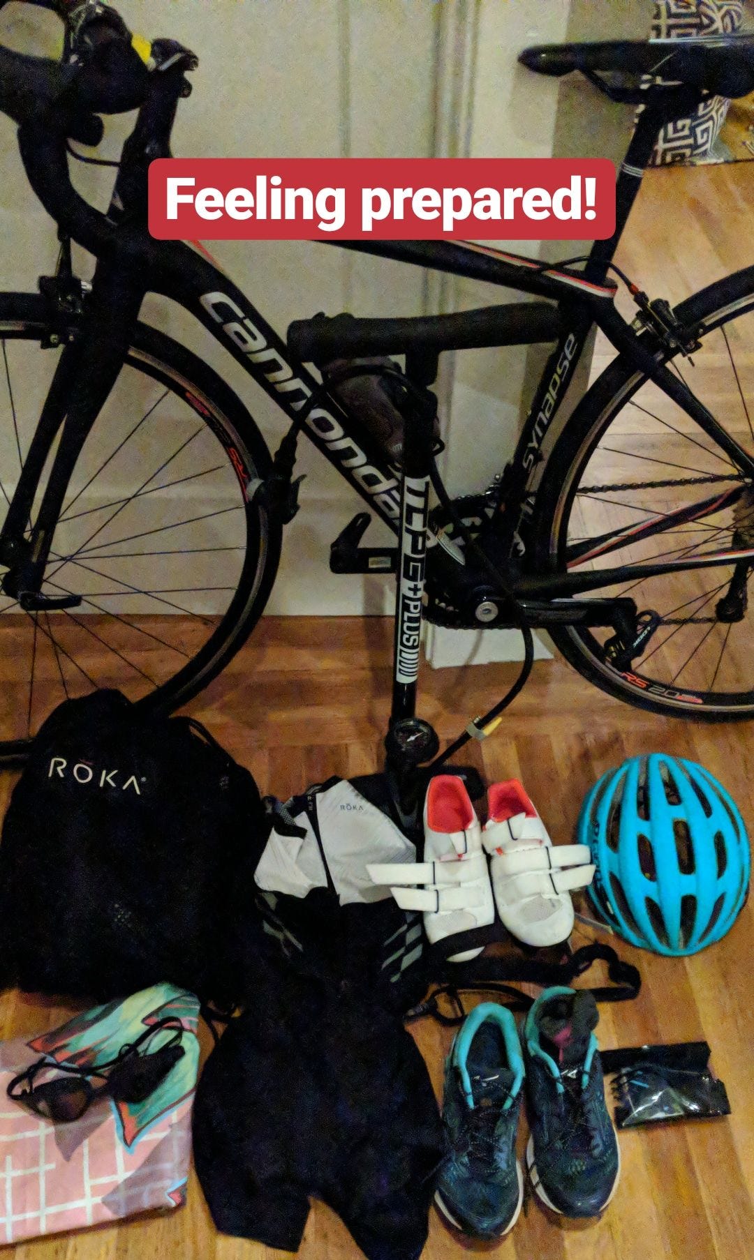 a triathlon bike resting against a bedroom wall with shoes, helmet, and goggles on the floor next to it. Text says Feeling Prepared!